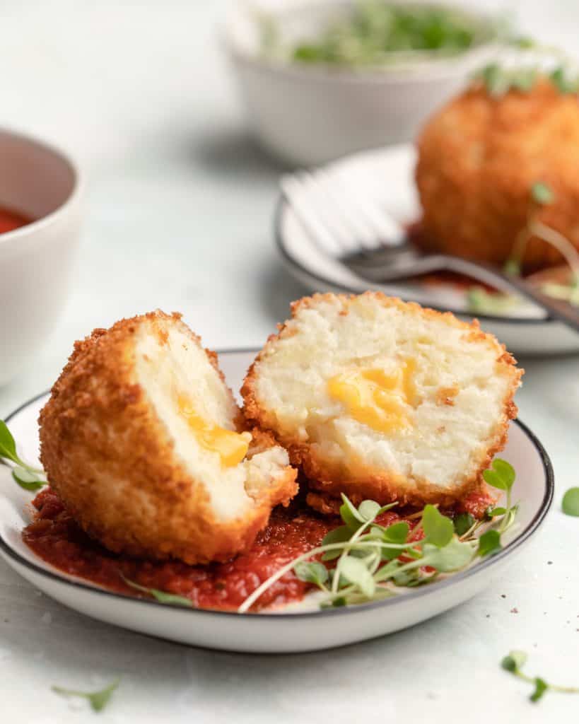 a fried ball of mashed potatoes filled with cheese on a small plate with marniara