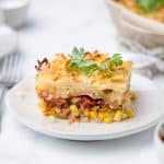 A piece of casserole with corn, bacon and shredded potatoes on a white plate with a fork and salsa.