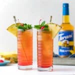 two tall glasses of iced tea with pineapple, cherry and mint garnish