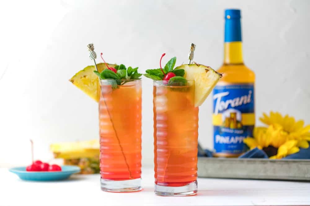 two tall glasses of iced tea with pineapple, cherry and mint garnish