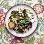 Salad with mushrooms and butter lettuce on a white plate and a floral tablecloth with mustard vinaigrette