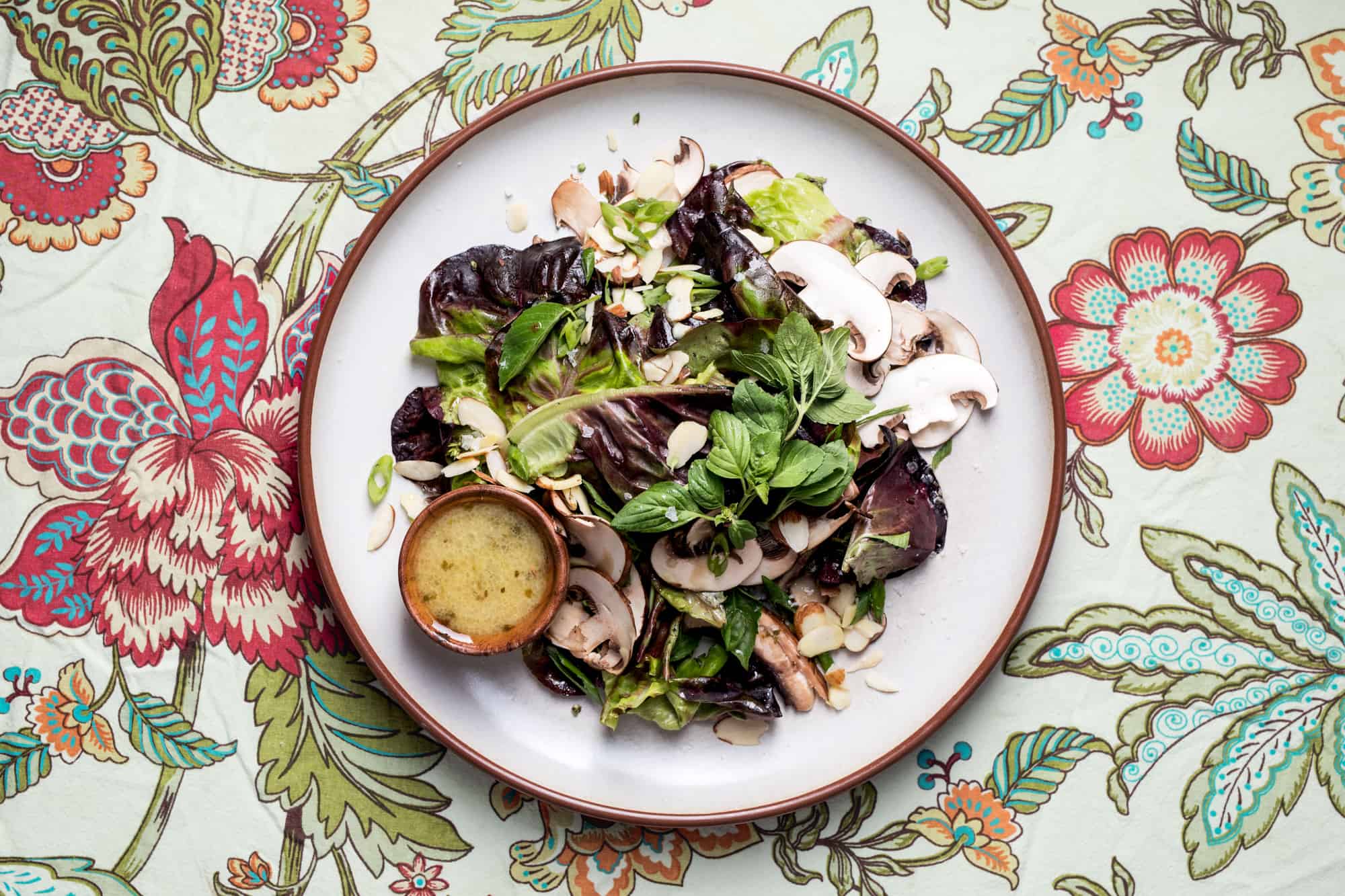 Salad with mushrooms and butter lettuce on a white plate and a floral tablecloth with mustard vinaigrette