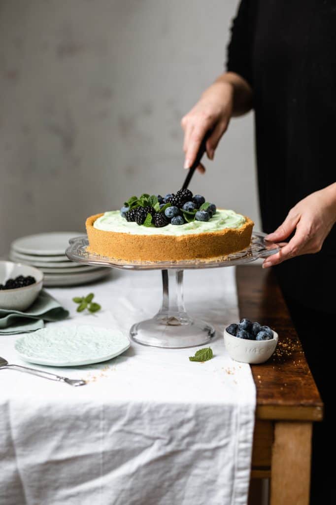 slicing into a pistachio tart on a wooden table with a white table cloth