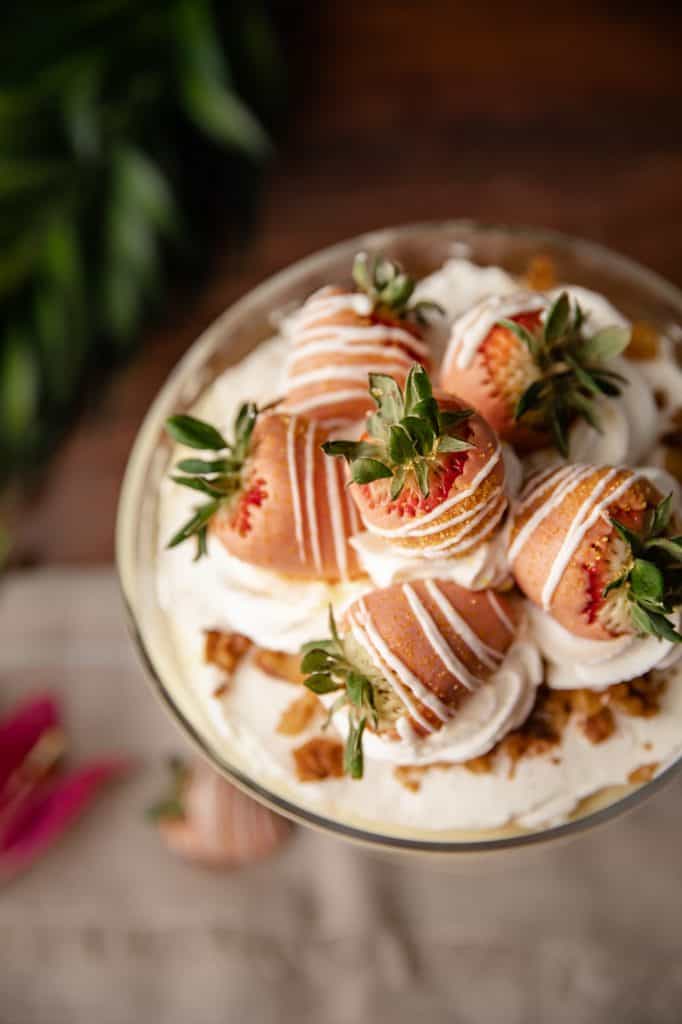 Overhead view of a trifle dish filled with homemade carrot cake, cream cheese whip and vanilla pudding topped with more whipped cream and dipped strawberries