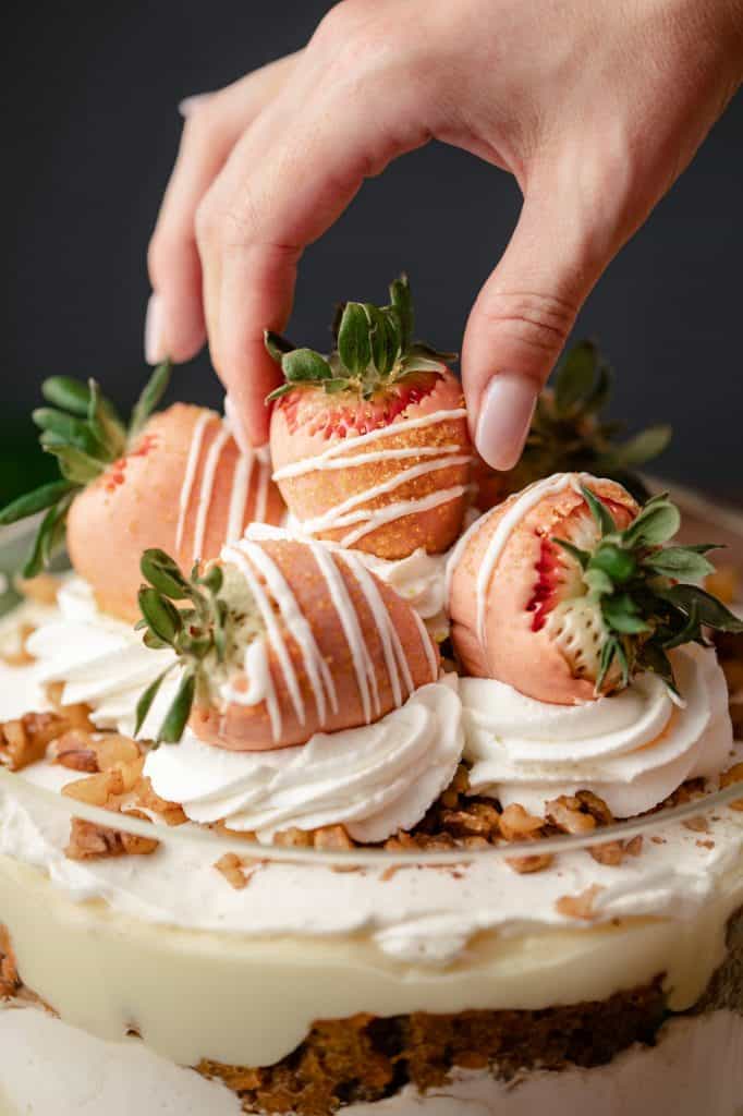 A trifle dish filled with homemade carrot cake, cream cheese whip and vanilla pudding topped with more whipped cream and dipped strawberries close up