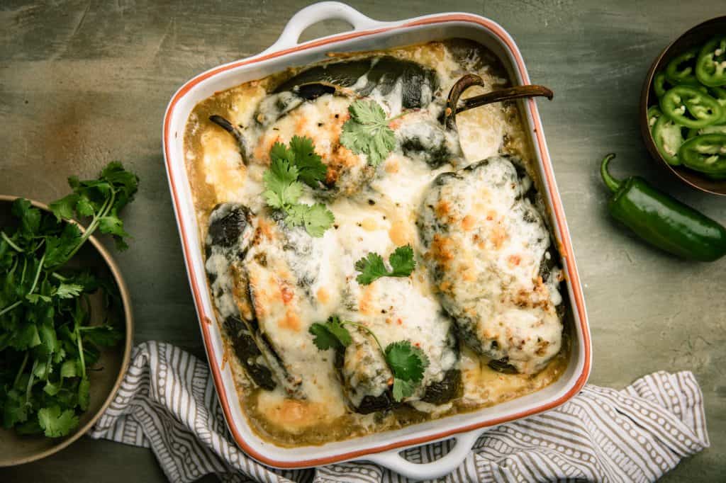 An overhead view of a casserole dish filled with stuffed peppers topped with white melted cheese, green chile salsa and cilantro