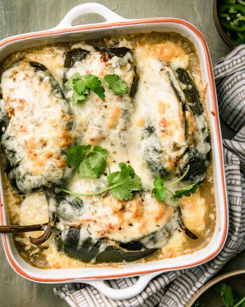 An overhead view of a casserole dish filled with stuffed peppers topped with white melted cheese, green chile salsa and cilantro