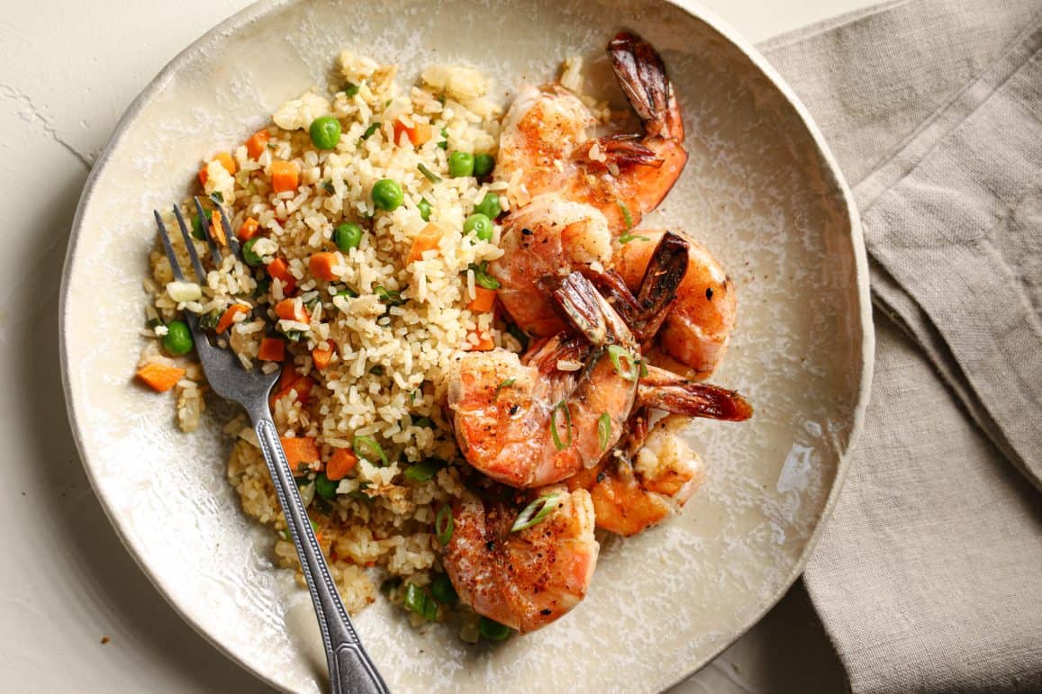Shrimp and fried rice on a tan plate with a napkin and fork
