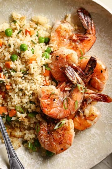 Shrimp and fried rice on a tan plate with a napkin and fork