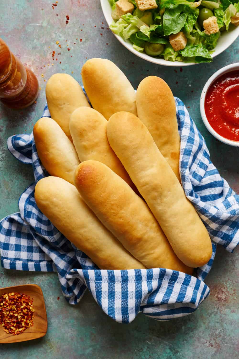 Overhead view of sourdough discard breadsticks in a basket with marinara sauce and salad.