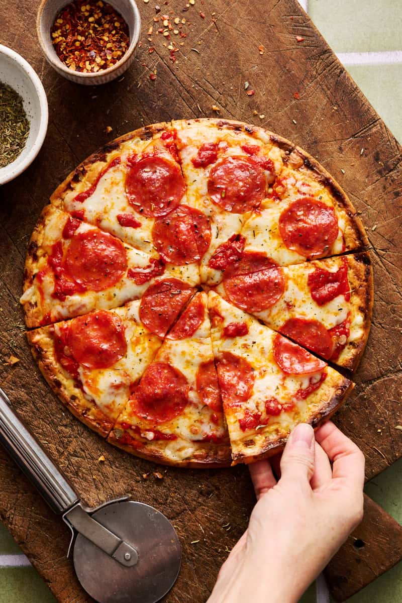 a sliced pizza with cottage cheese crust and a hand grabbing a slice