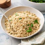 Fonio pilaf in a serving bowl garnished with herbs