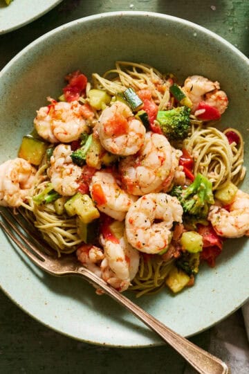 Veggie shrimp pasta plated in bowls with extra lemon and parmesan on the side