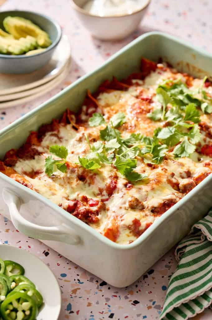 Ground Beef Enchiladas with a serving removed and plated along with fresh jalapenos and avocado