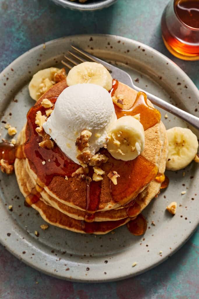 a stack of banana protein pancakes topped with nuts, bananas and greek yogurt for more stable blood sugar