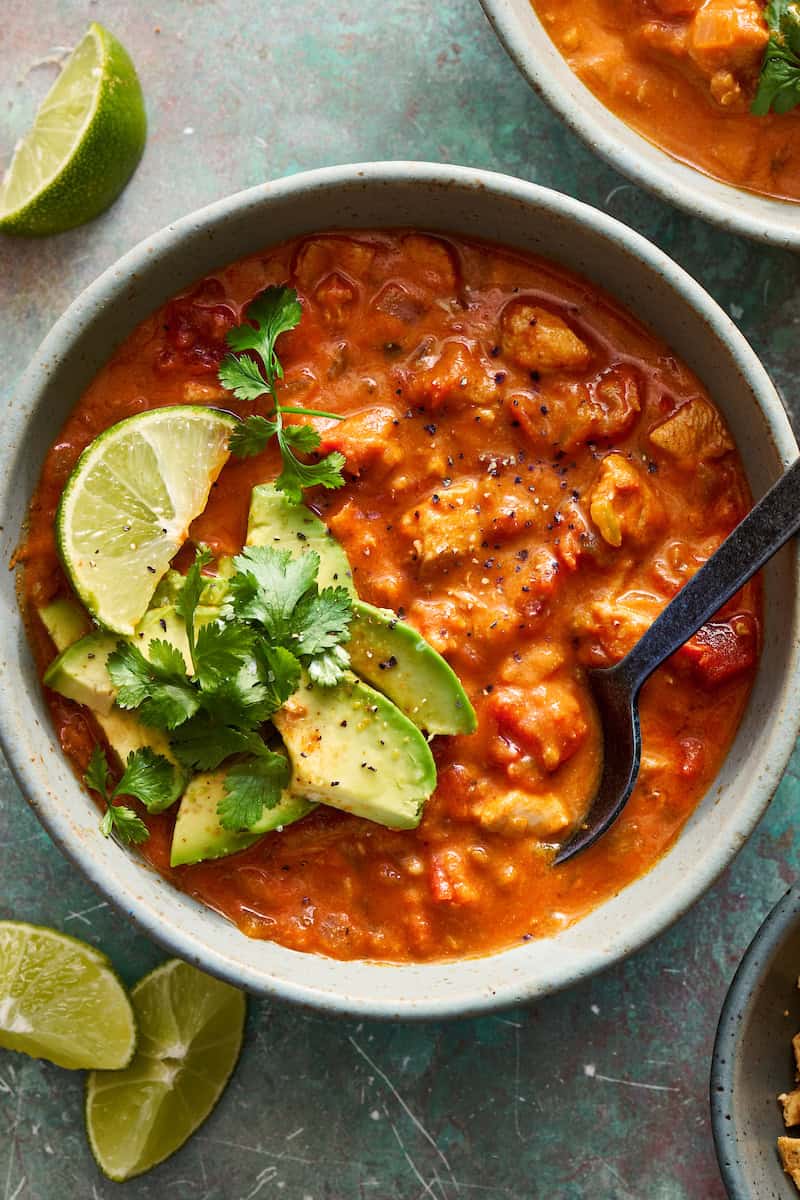 a bowl of chicken enchilada soup dressed with avocado and lime