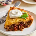 a slice of taco pie on a plate topped with cilantro and sour cream