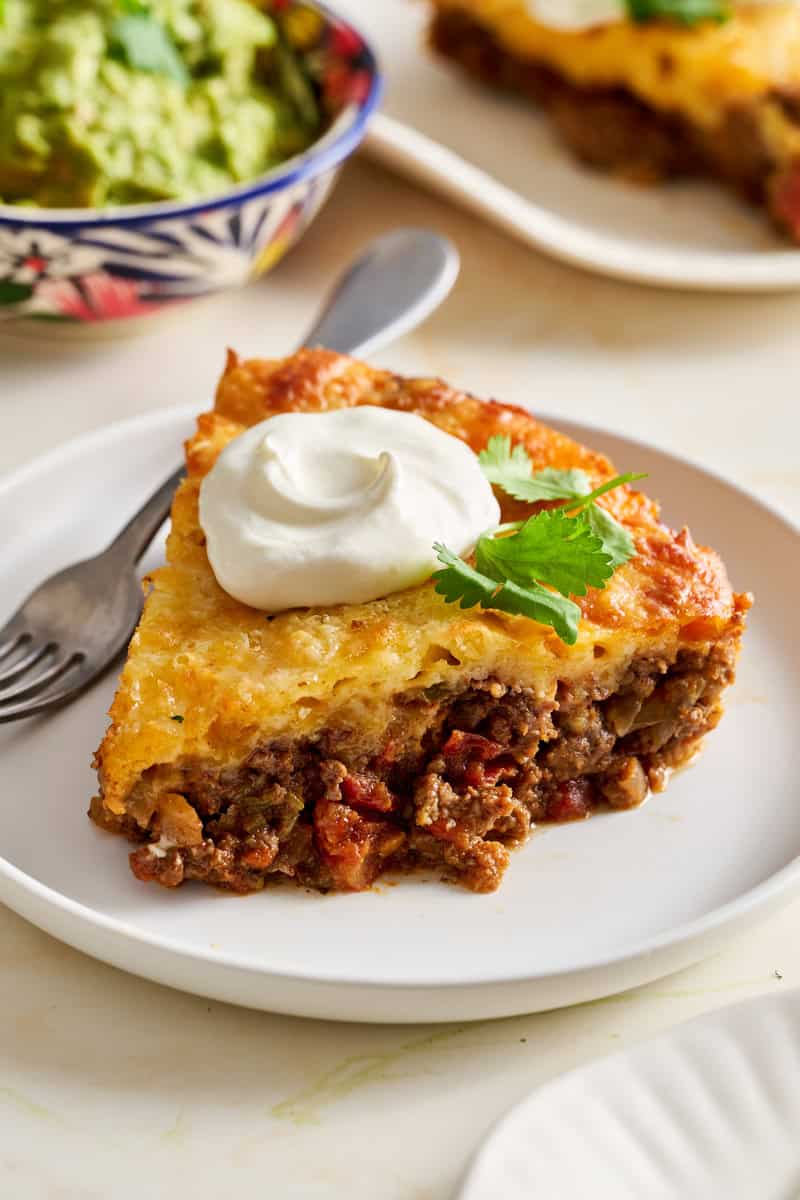 a slice of taco pie on a plate topped with cilantro and sour cream