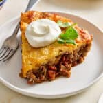a slice of taco pie on a plate topped with cilantro and sour cream