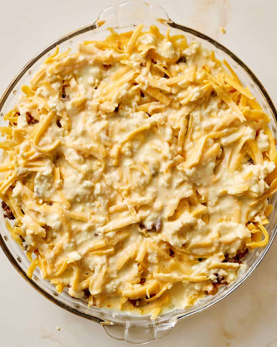 adding the taco meat to the pan and topping it with the biscuit mixture folded with cheese