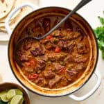 cast iron dutch oven with carne guisada and tortillas on the side