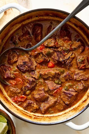 cast iron dutch oven with carne guisada and tortillas on the side
