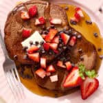 chocolate sourdough pancake stack with maple syrup and chocolate chips and diced strawberry