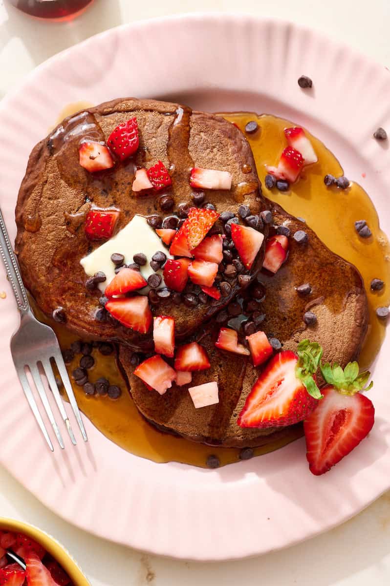 chocolate sourdough pancake stack with maple syrup and chocolate chips and diced strawberry