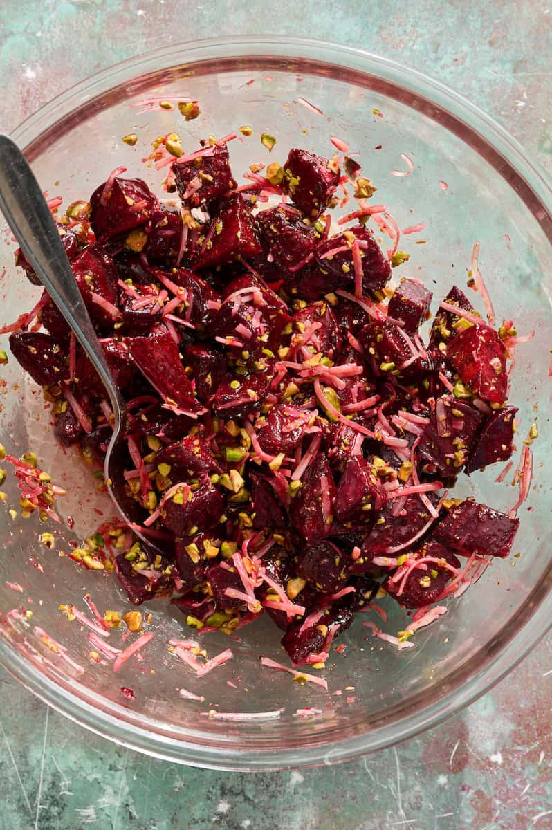 adding the dressing, parmesan and pistachios to the bowl with the beets